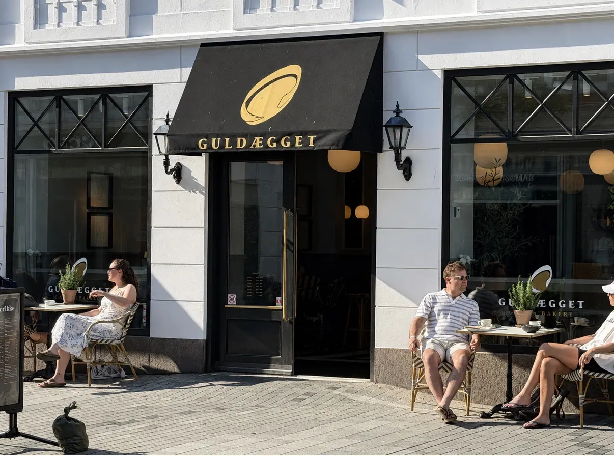 Café Guldæggets facade i Kongensgade med markise og gæster ved bordene i solen