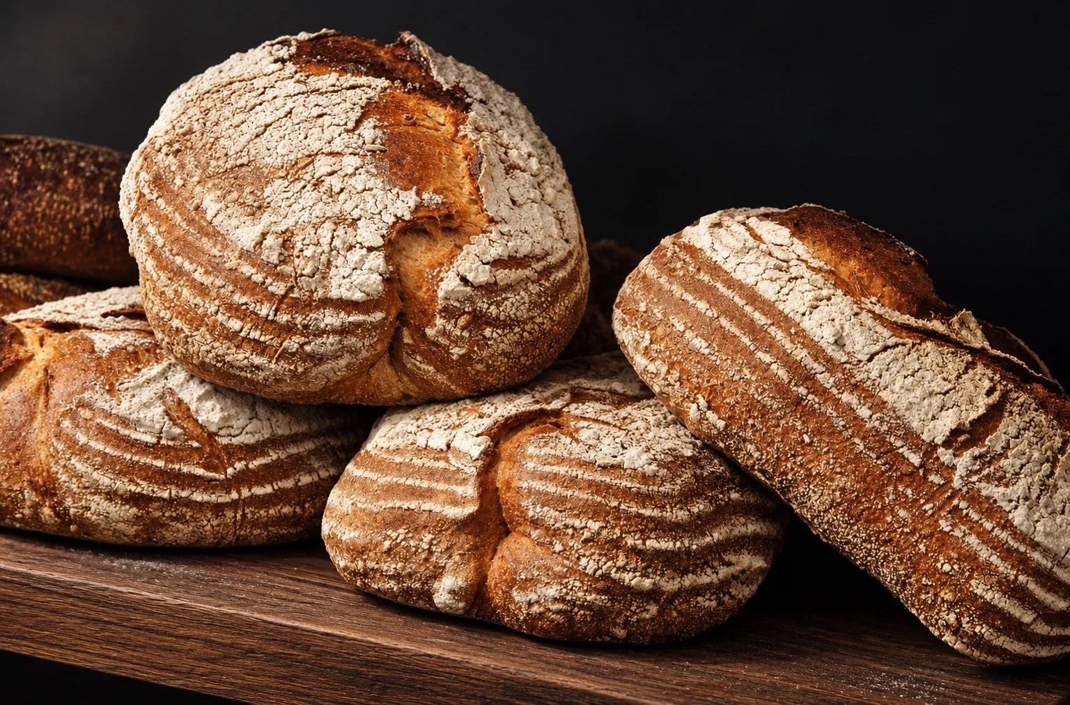 Friskbagte runde og aflange brød med sprøde, melede skorper på et mørkt træbræt